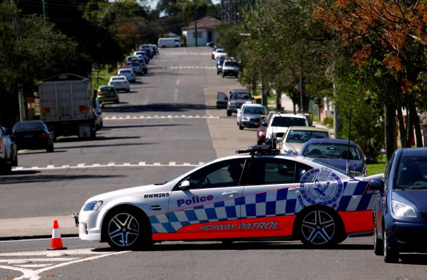 A policeman sits in his patrol car as part of a road block on the street where a house was involved in pre-dawn raids in the western Sydney suburb of Guilford