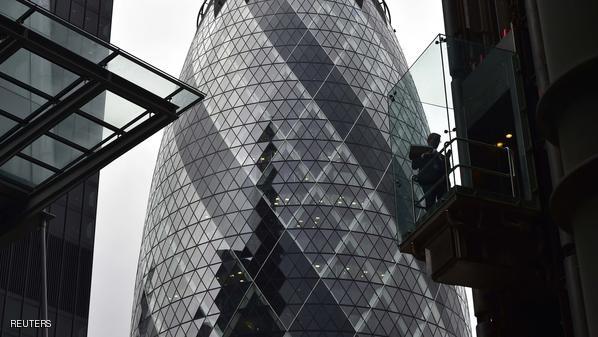 An employee is pictured in front of the 30 St Mary Axe skyscraper as he rides an elevator on the exterior of the Lloyd's of London building in London